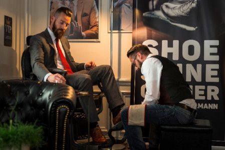 Claudio Bühlmann pflegt an einem Messestand die Schuhe eines Gastes im Chesterfield-Sessel